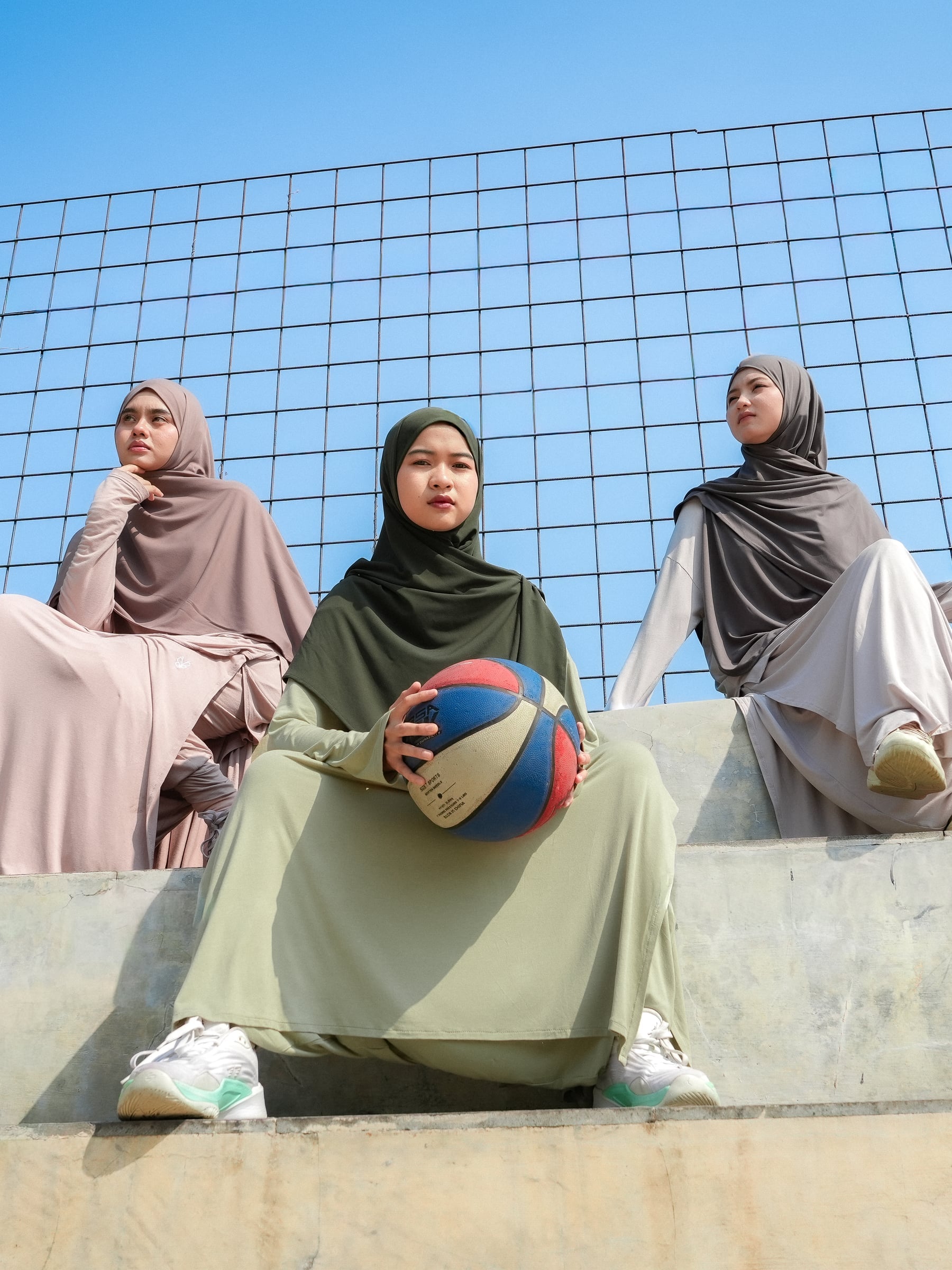 Tiga model mengenakan setelan sporty TAQA duduk di tribun lapangan basket